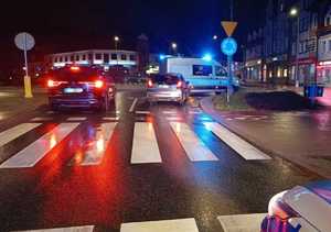Zabezpieczone miejsce zdarzenia-potrącenie pieszej na oznakowanym przejściu dla pieszych. Stojące na jezdni dwa pojazdy osobowe oraz radiowóz policyjny