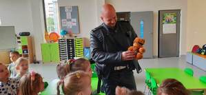 Policjant trzymający misiaczka rozrabiaczka któremu założył kajdanki w okół grupa przedszkolaków