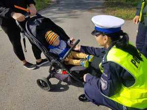 Policjantka przekazująca odblask dla dziecka siedzącego w wózku