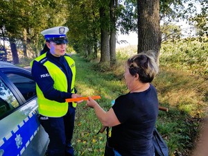 Policjantka przekazuje kobiecie kierującej rowerem opaskę odblaskową