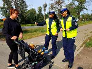 Policjantki przekazujące elementy odblaskowe kobiecie i dziecku siedzącemu w wózku