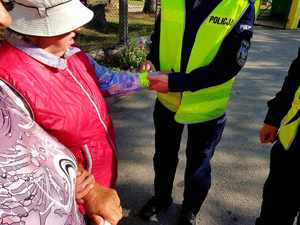 policjantka zakładająca opaskę odblaskową pieszej uczestniczce ruchu drogowego