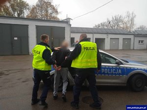 policjanci prowadzą zatrzymanego w tle policyjny radiowóz