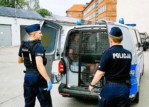 Zatrzymany mężczyzna w radiowozie , przed radiowozem umundurowani policjanci