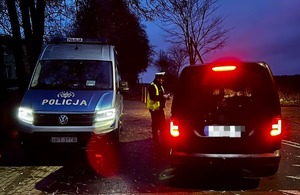 Policjant sprawdzający stan trzeźwości kierującego pojazdem osobowym, w oddali radiowóz