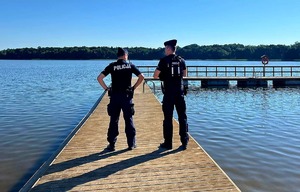 Policjanci stojący na pomoście wokół woda a w oddali las