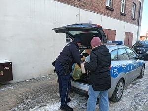 Policjant oraz pracownik MOPS wyjmują artykuły z radiowozu dla osoby potrzebującej