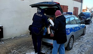 Policjant oraz pracownik MOPS wyjmują artykuły z radiowozu dla osoby potrzebującej